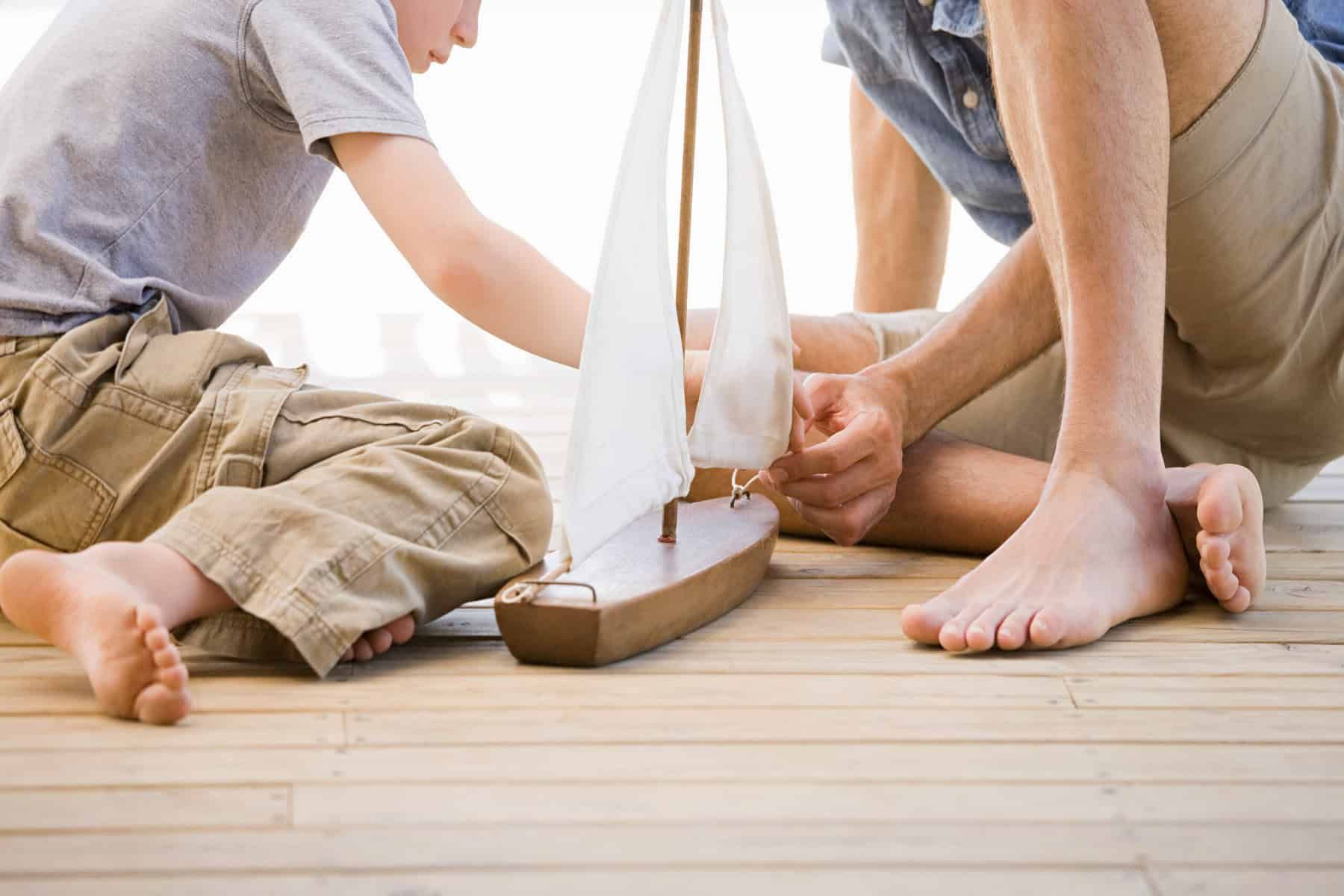 Two people building a model sailboat together on a wooden surface.