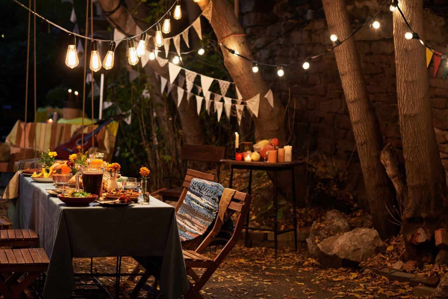 Outdoor dinner party at night with string lights, bunting, and food on a long table.