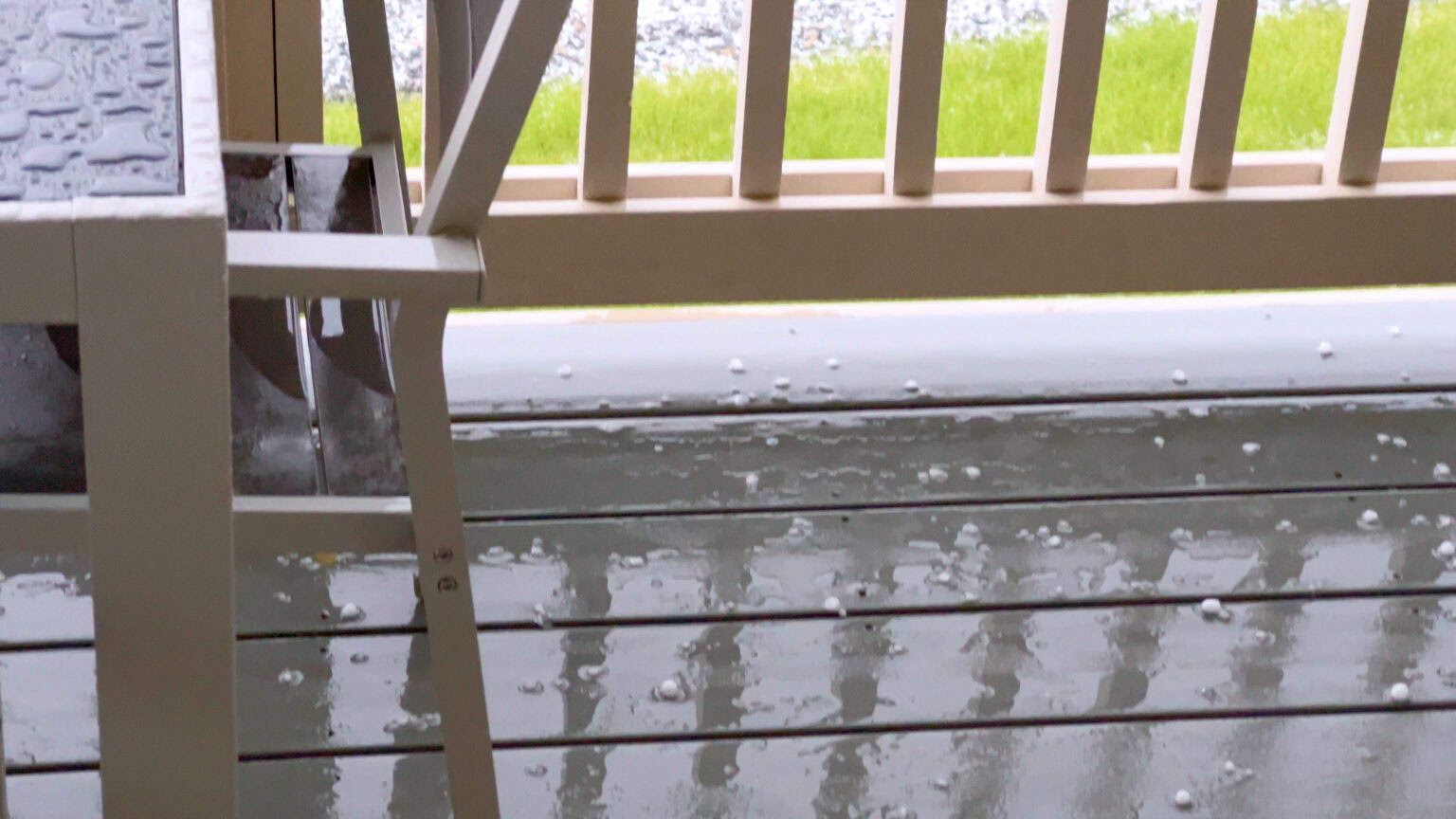Hail covering a wooden deck, with a railing and partial view of grass.