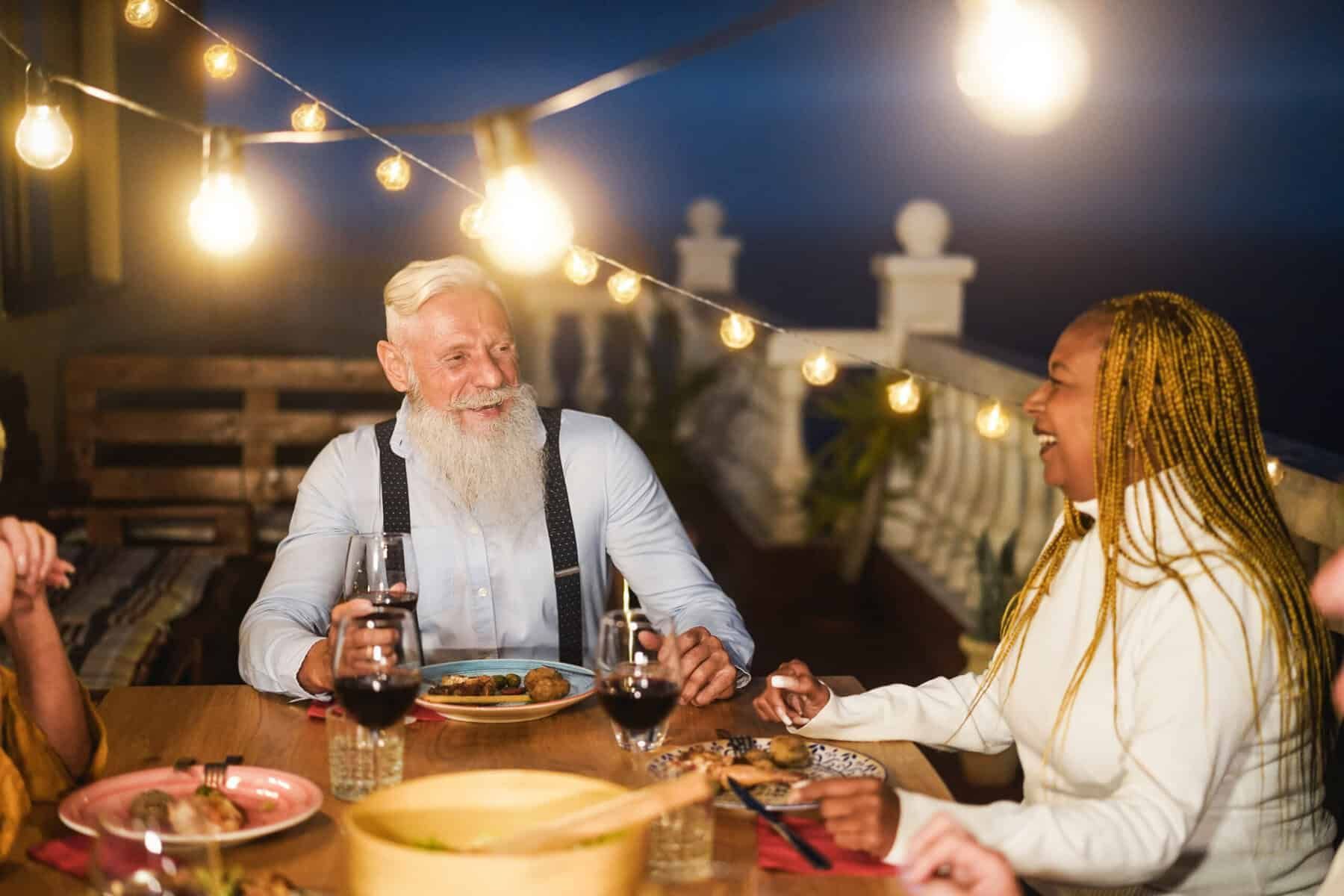 People enjoying a meal at an outdoor table at night, illuminated by string lights.
