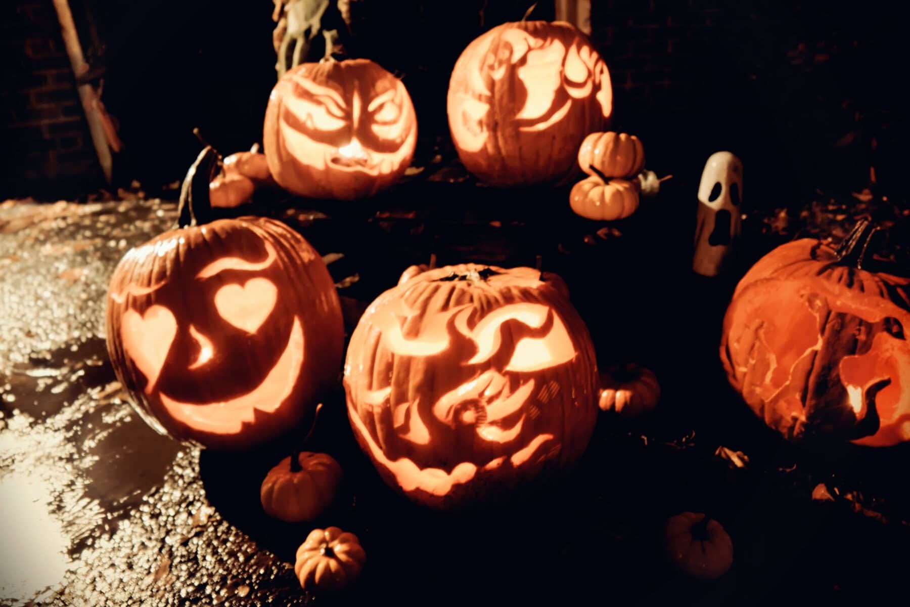 Glowing carved pumpkins with various faces, lit at night for Halloween.