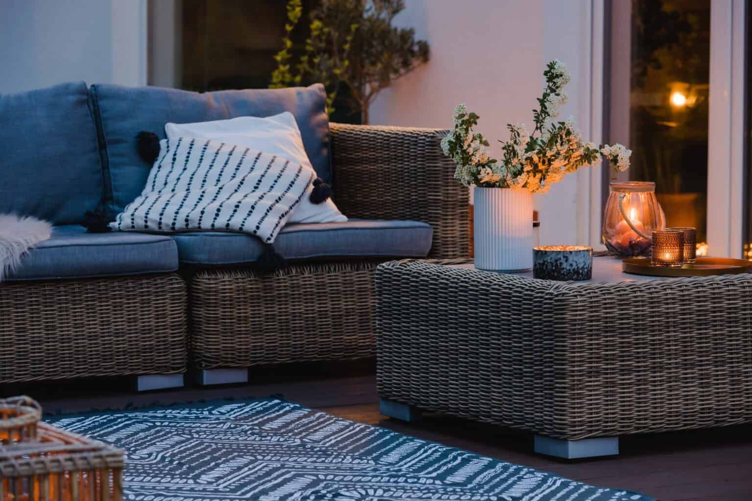 Wicker patio furniture with blue cushions and decorative pillows. Coffee table with flowers and candles.