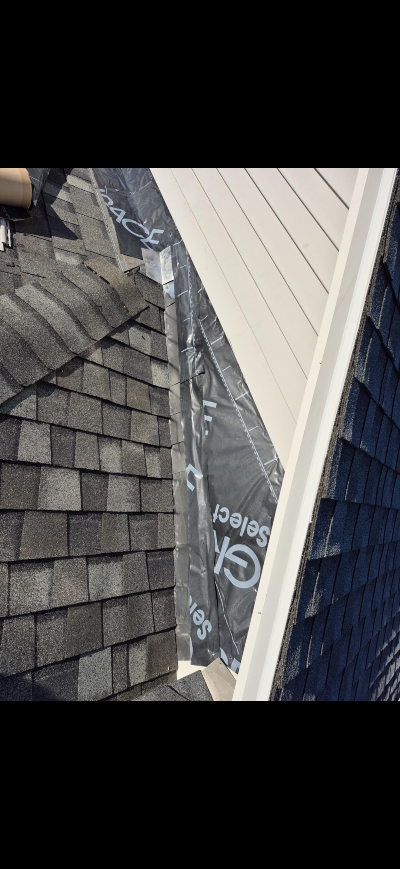 Close-up of a new roof installation: shingles meeting siding, with underlayment visible.