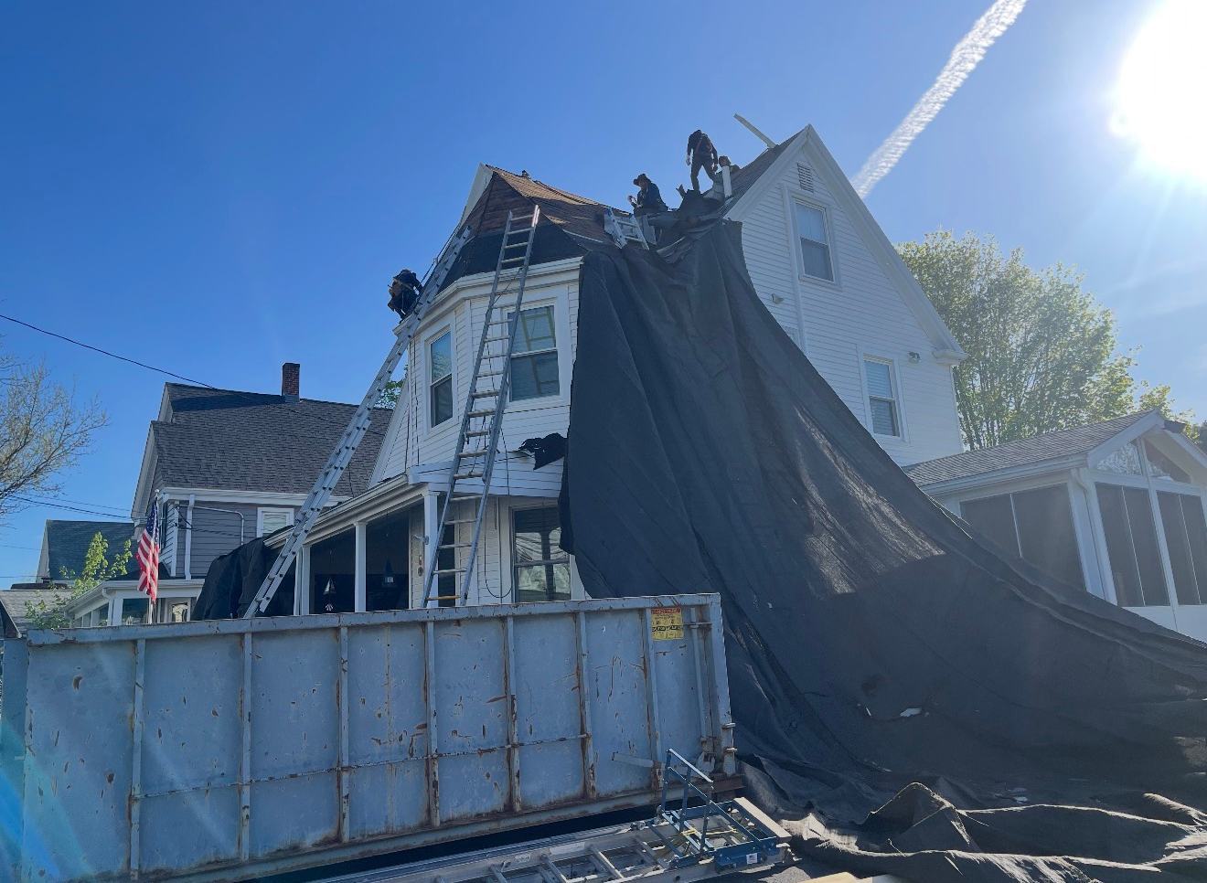 Roofers working on a house with a tarp over the roof; a dumpster is at the base of the house.
