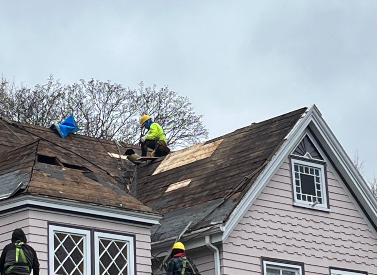 Roofers repairing a pink house with damaged shingles on a cloudy day.