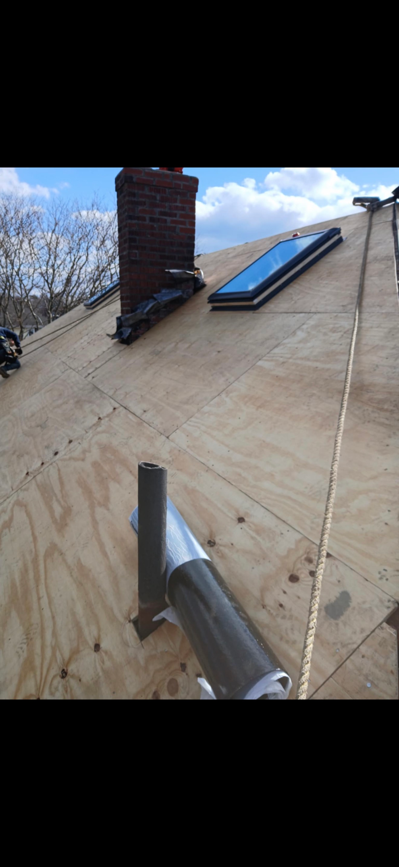 A rooftop with a chimney, a skylight, and metal pipes against a cloudy sky.