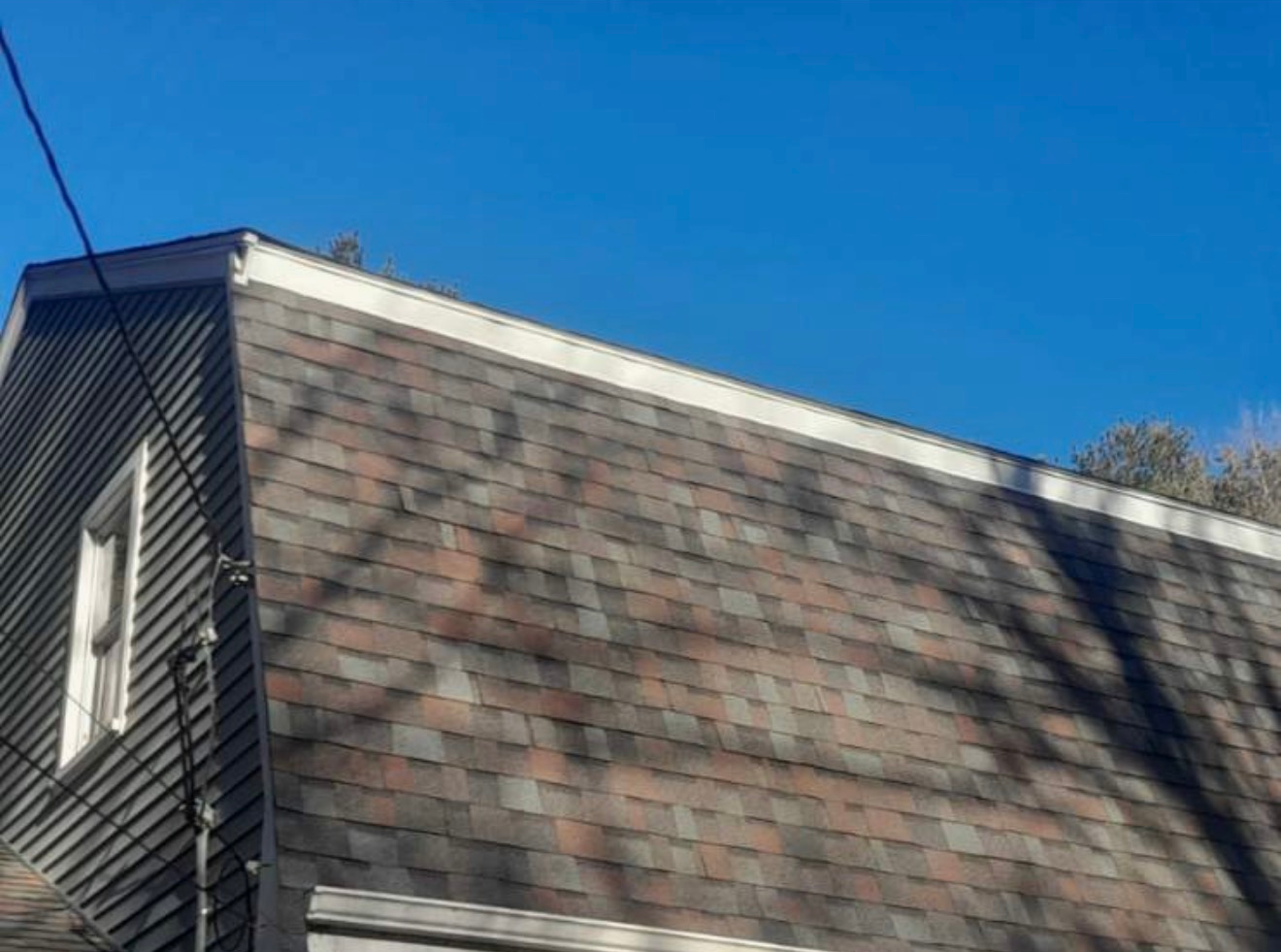 A house with an asphalt shingle roof on a bright blue sky day.
