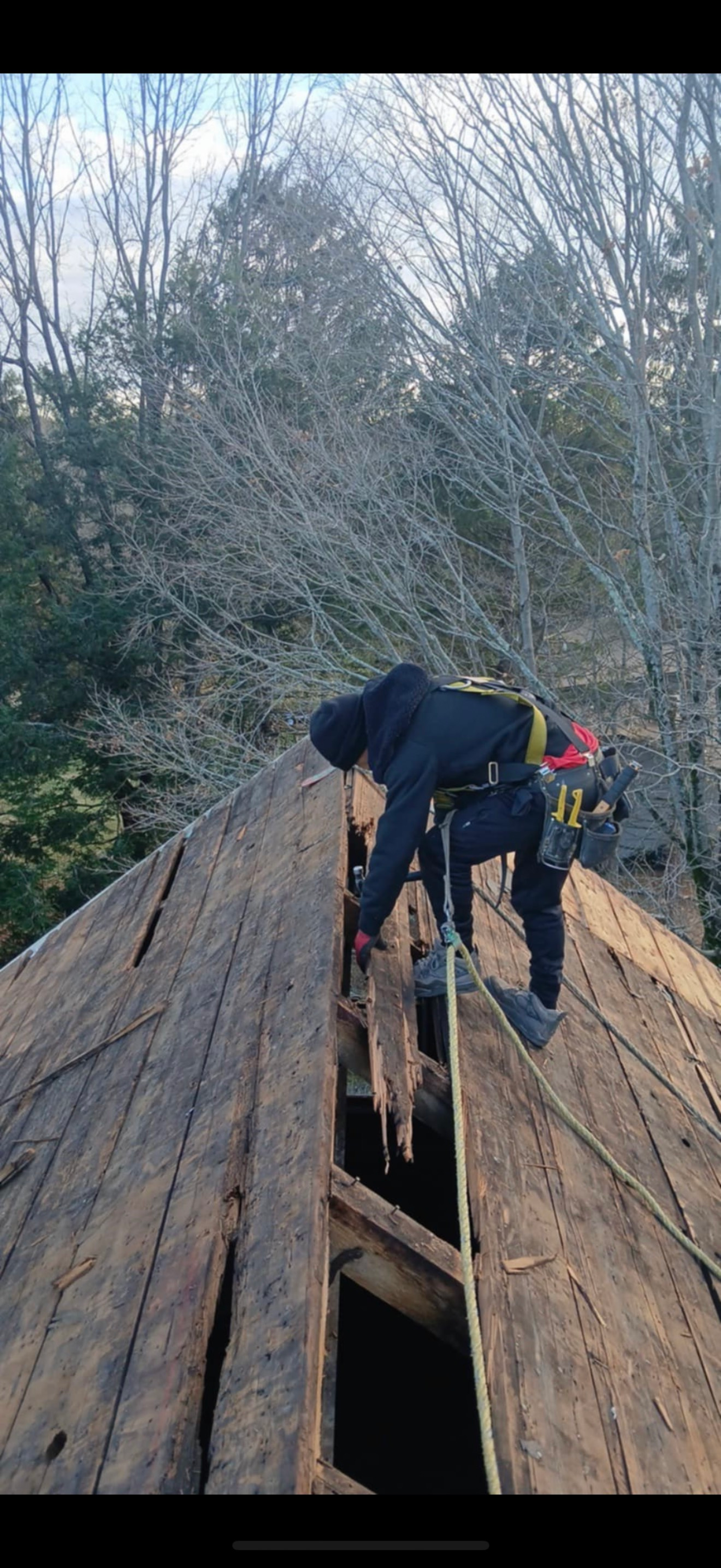 Person on a rooftop, working on exposed wooden beams, with safety equipment.