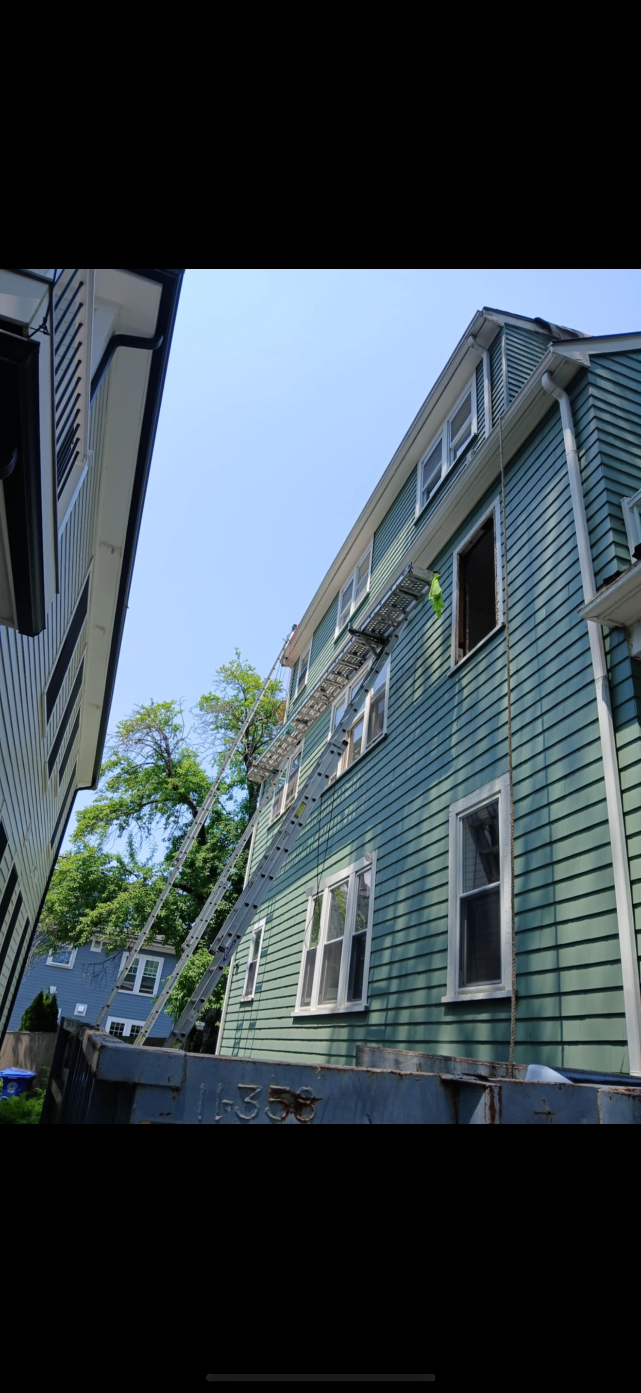 A teal building with a fire escape. A tall ladder is propped against the building, and the sky is clear.
