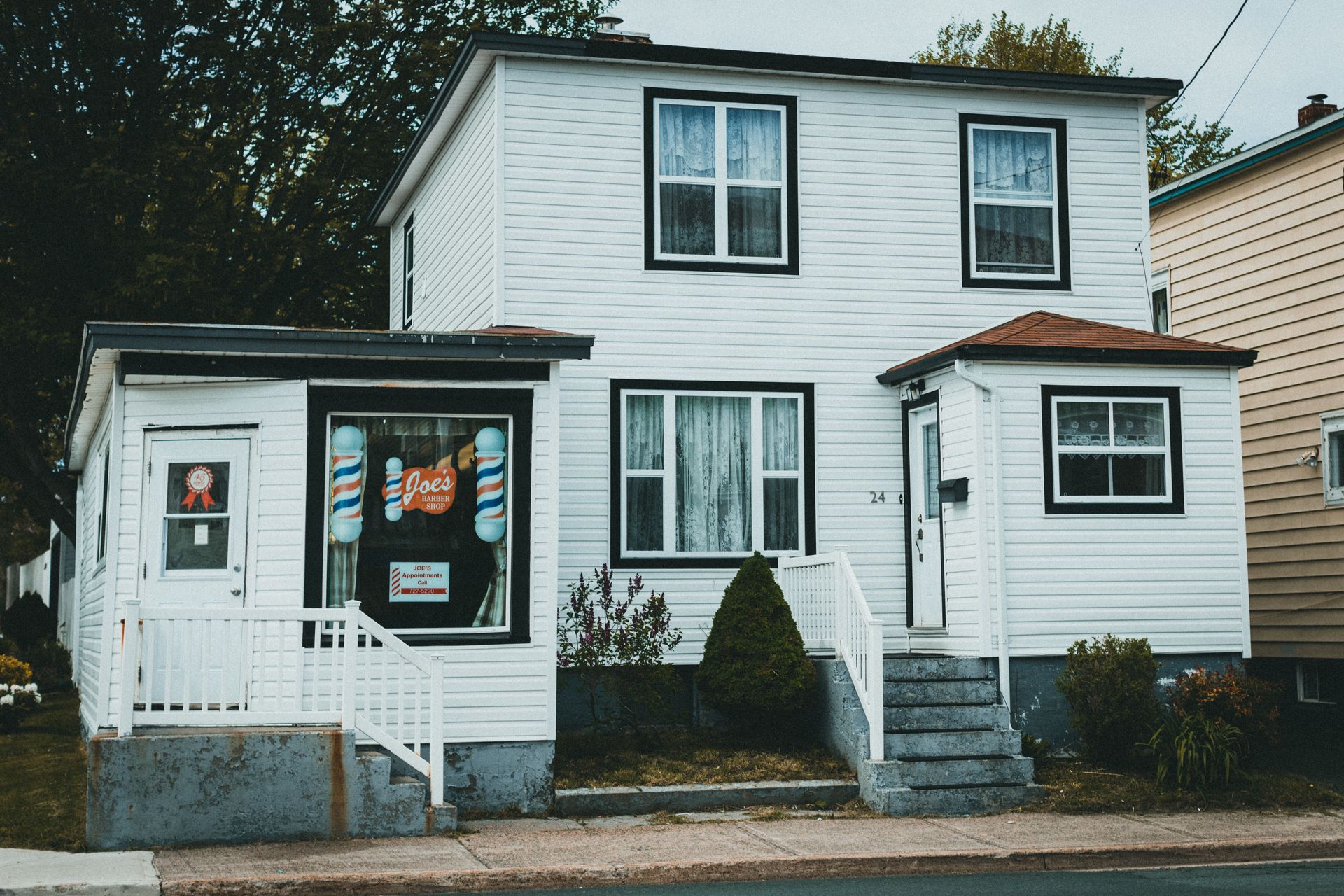 White two-story house with dark trim, front porch, and steps beside a neighboring home.