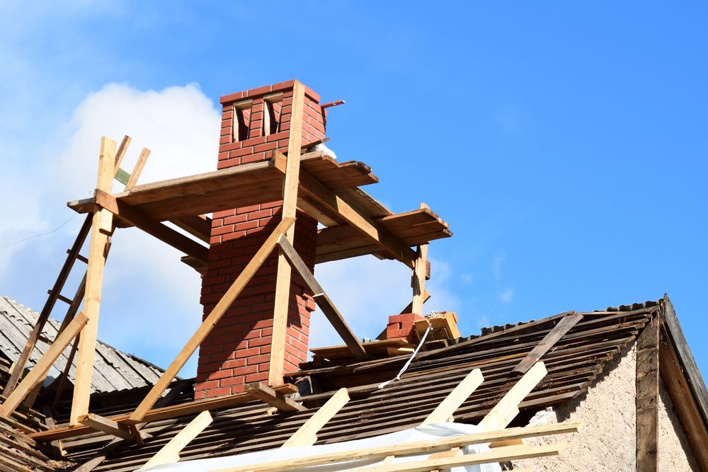 Chimney being repaired on a roof, wooden scaffolding is set up against the red brick stack.