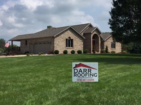 A large brick house with a darr roofing sign in front of it