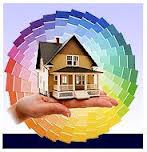 A person is holding a model house in front of a rainbow of paint samples.