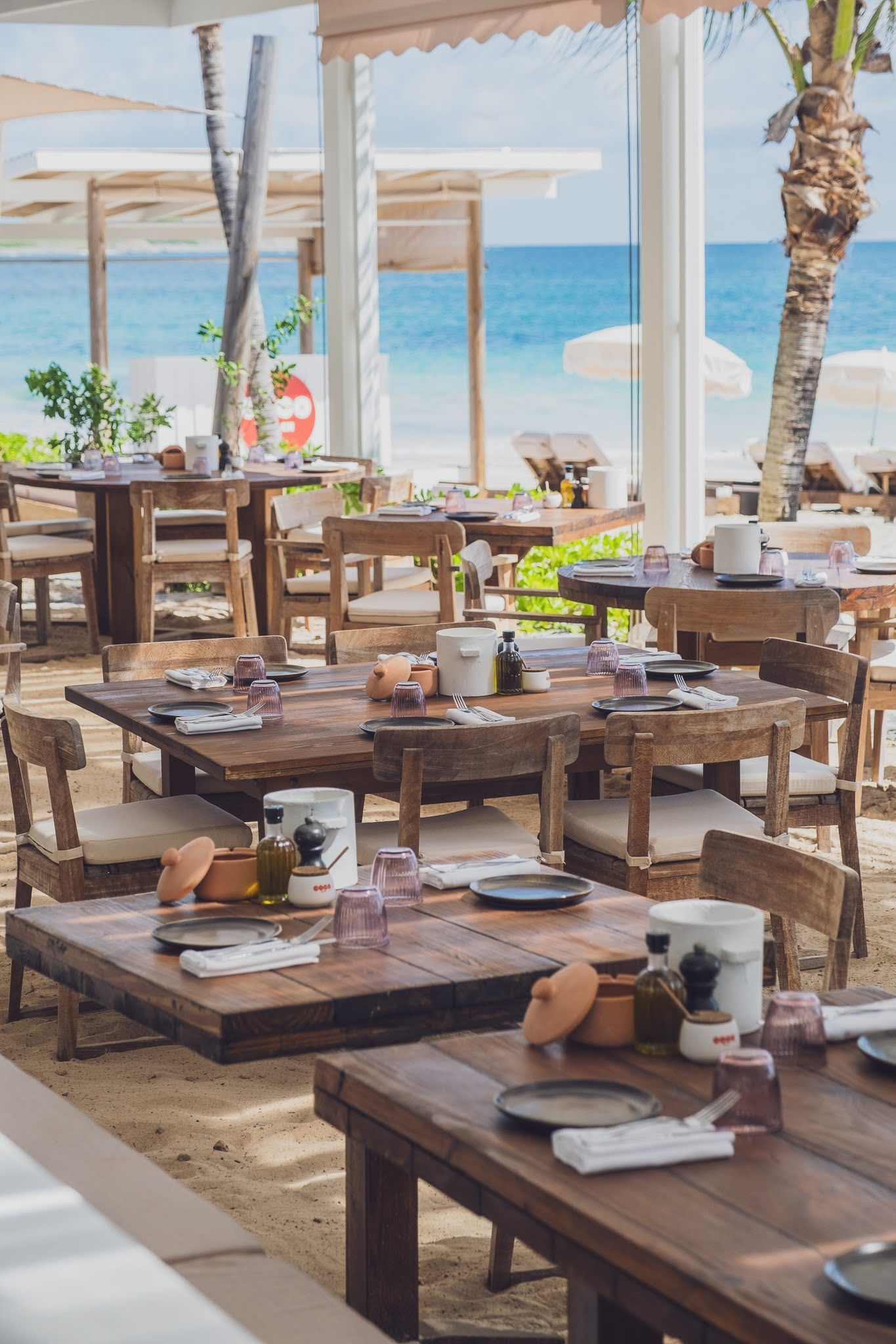 Beachside restaurant with wooden tables and chairs, ocean view.