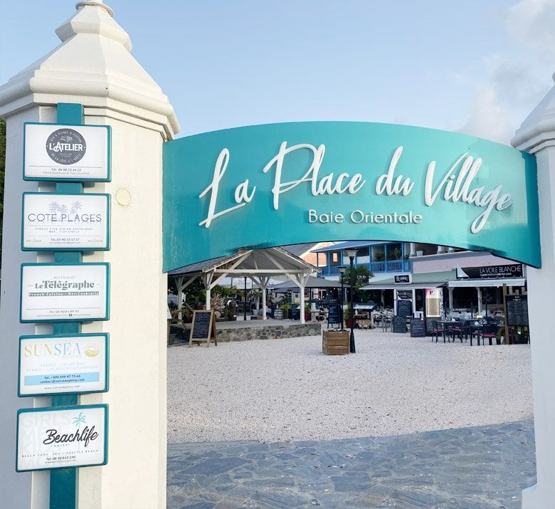 Entrance to La Place du Village in Orient Bay, Saint Martin, with turquoise archway and restaurant signs.