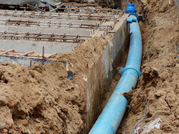 A blue pipe is laying in the dirt next to a concrete wall.