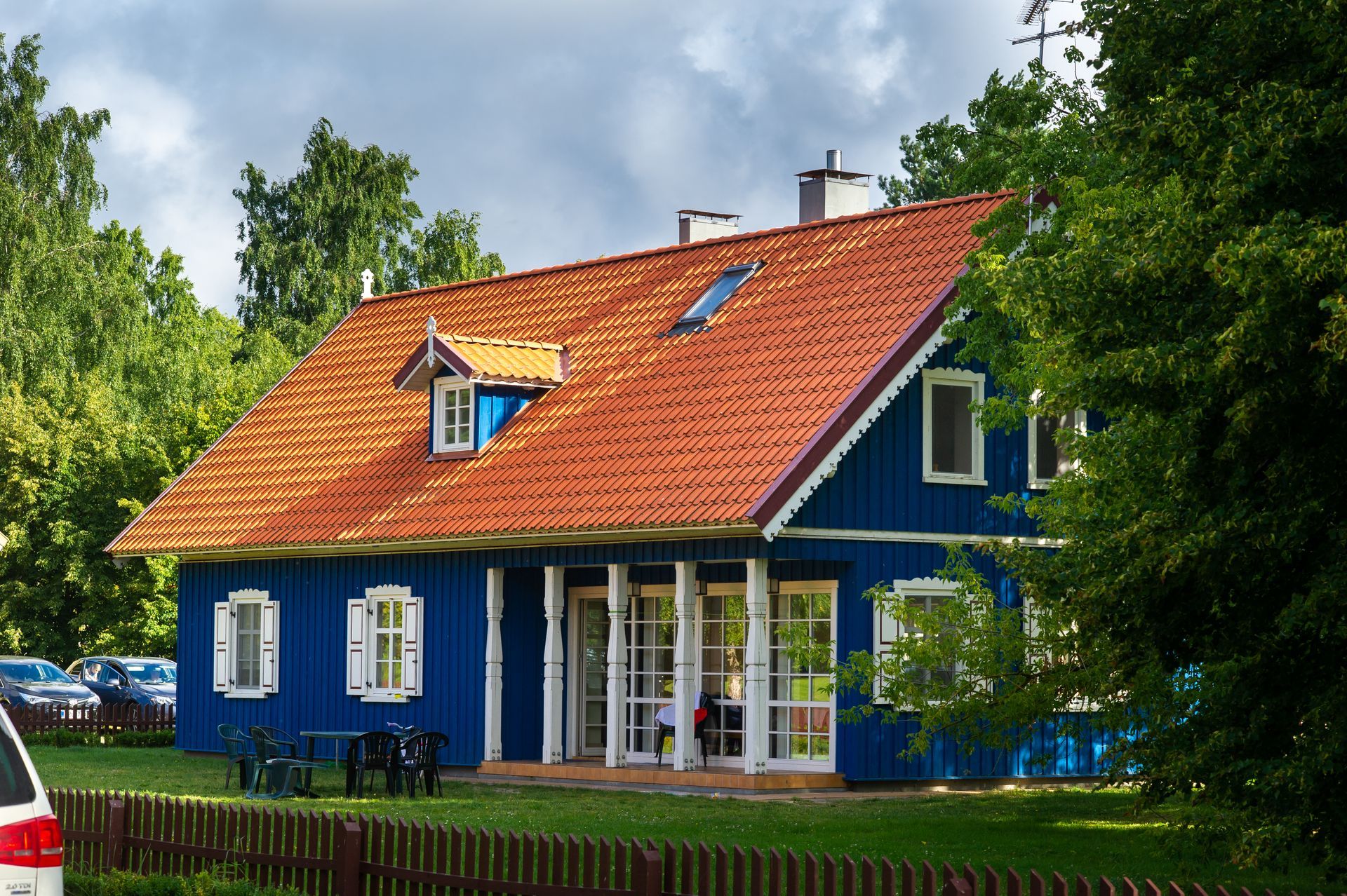 Blue wooden house with a red roof, white trim, and a green lawn under a cloudy sky.