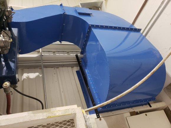 Blue industrial ductwork bends at a right angle, bolted to a wall.