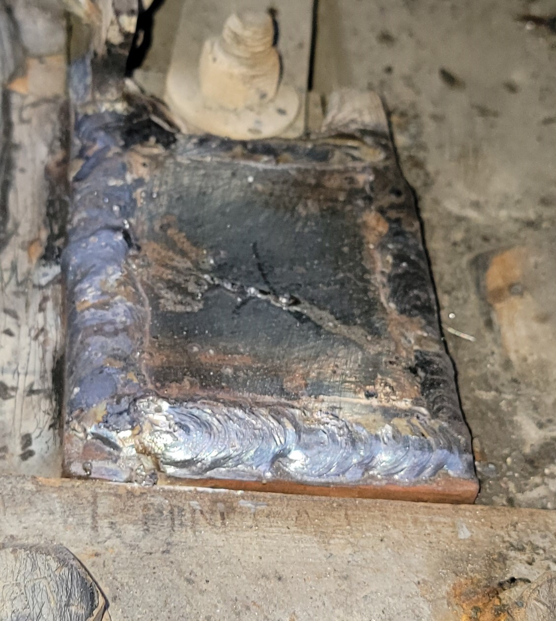 Welded metal plate with visible crack, attached to a vehicle component.