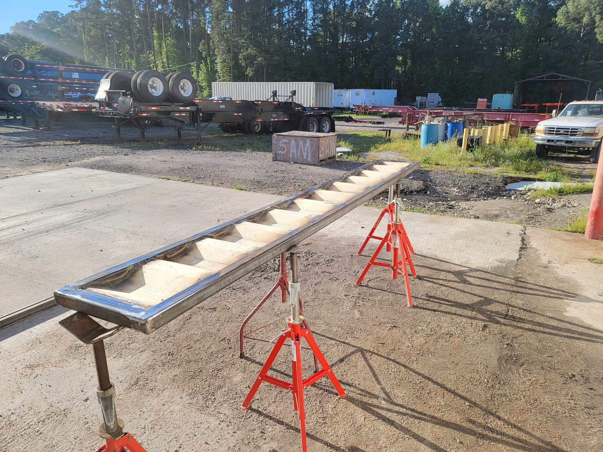 Long metal trough filled with sand, supported by red sawhorses outdoors.