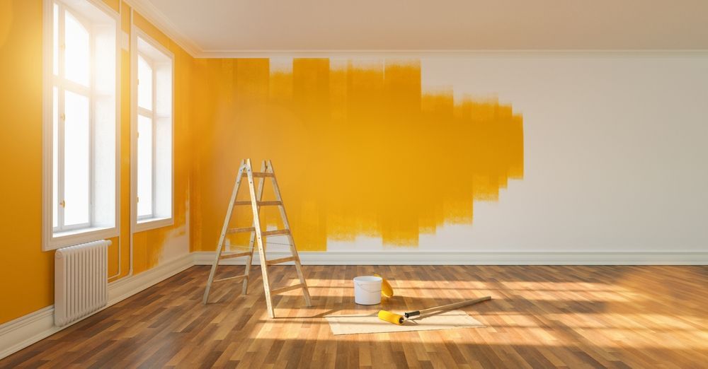 An empty room with yellow walls and a wooden floor is being painted.