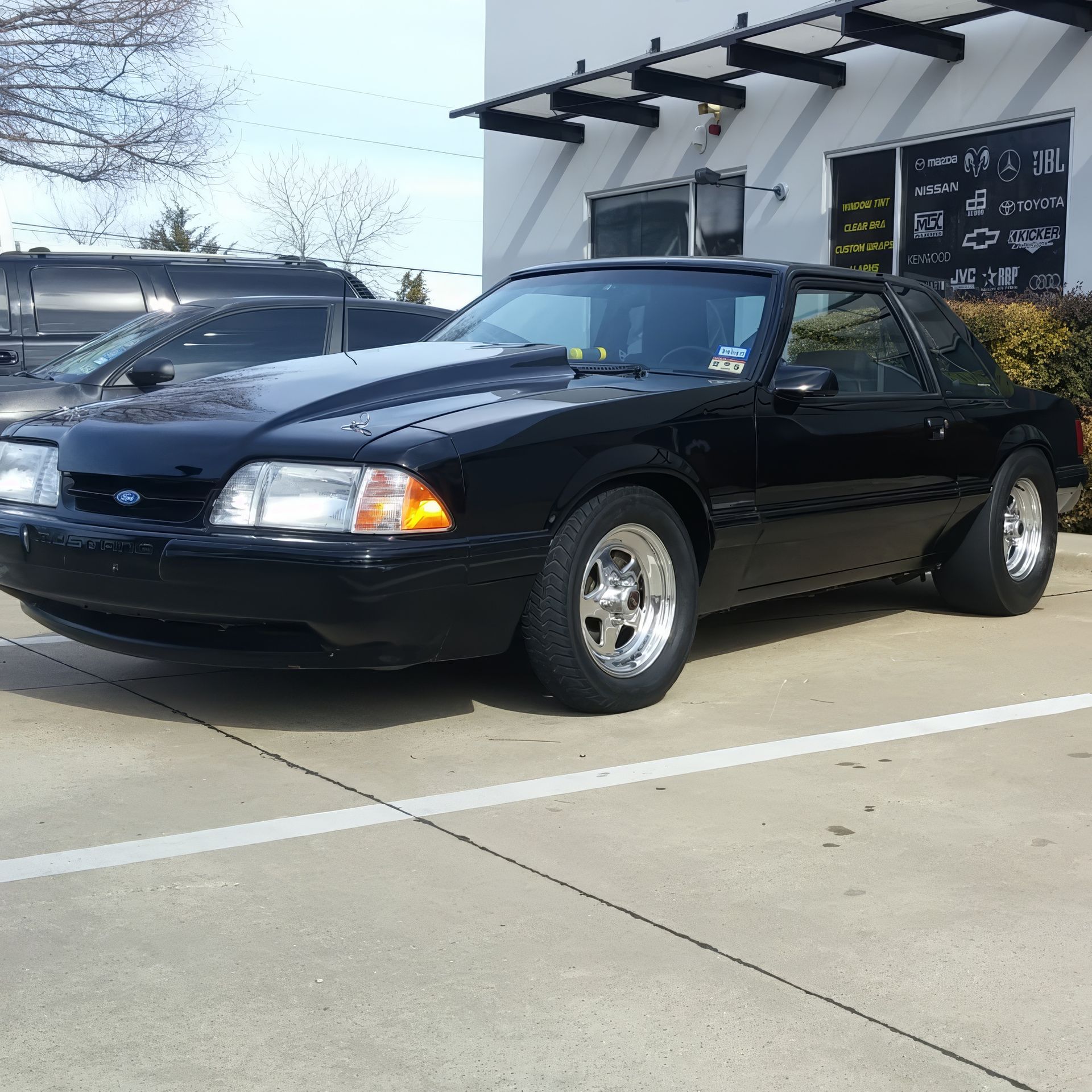 Black convertible parked in a lot beside a building, viewed from the front-left side.