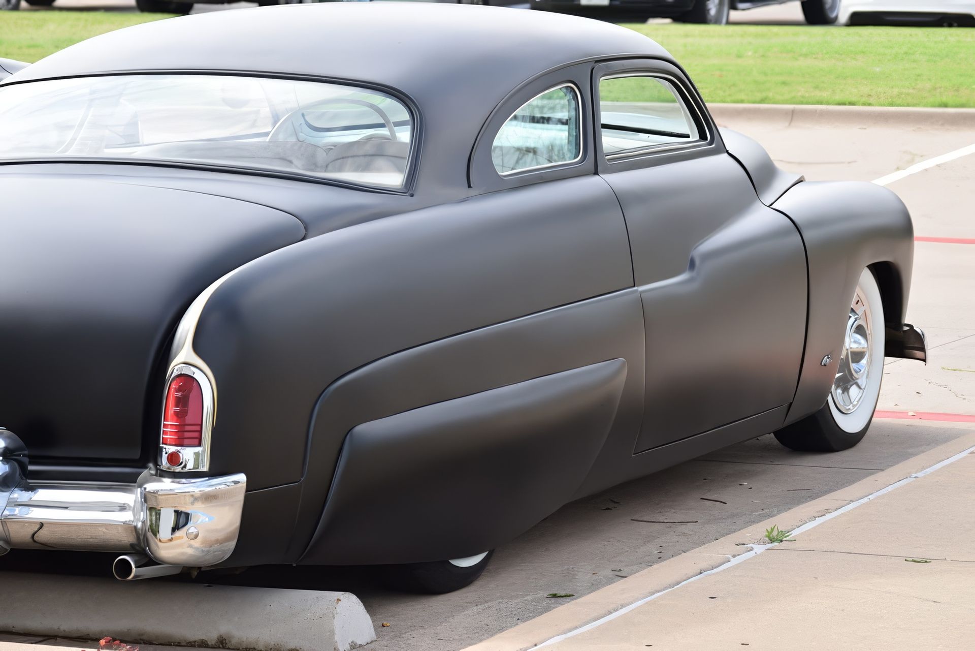 Matte black vintage coupe with custom lowered body parked on a street curb