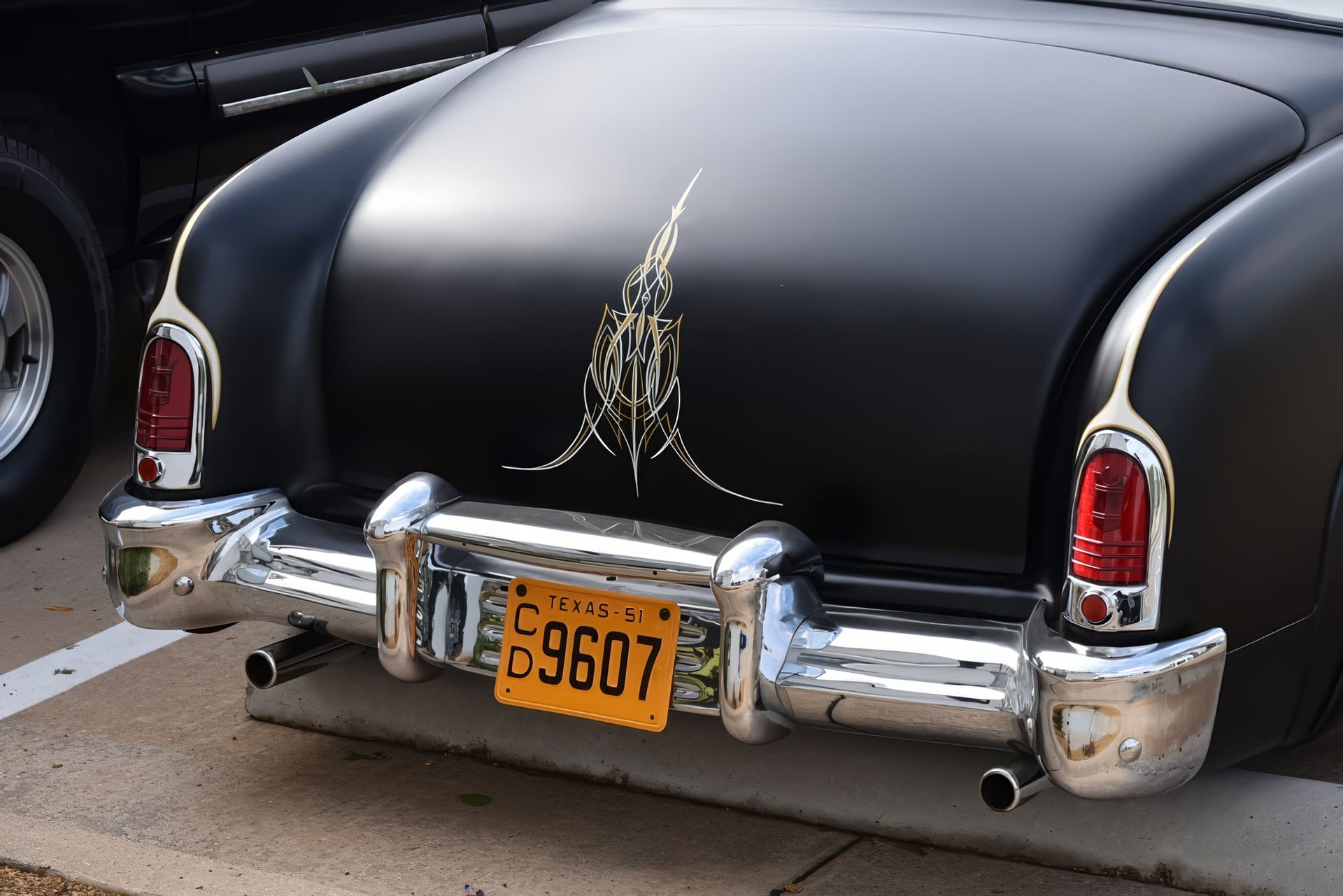 Rear view of a black vintage car with chrome bumper and yellow license plate