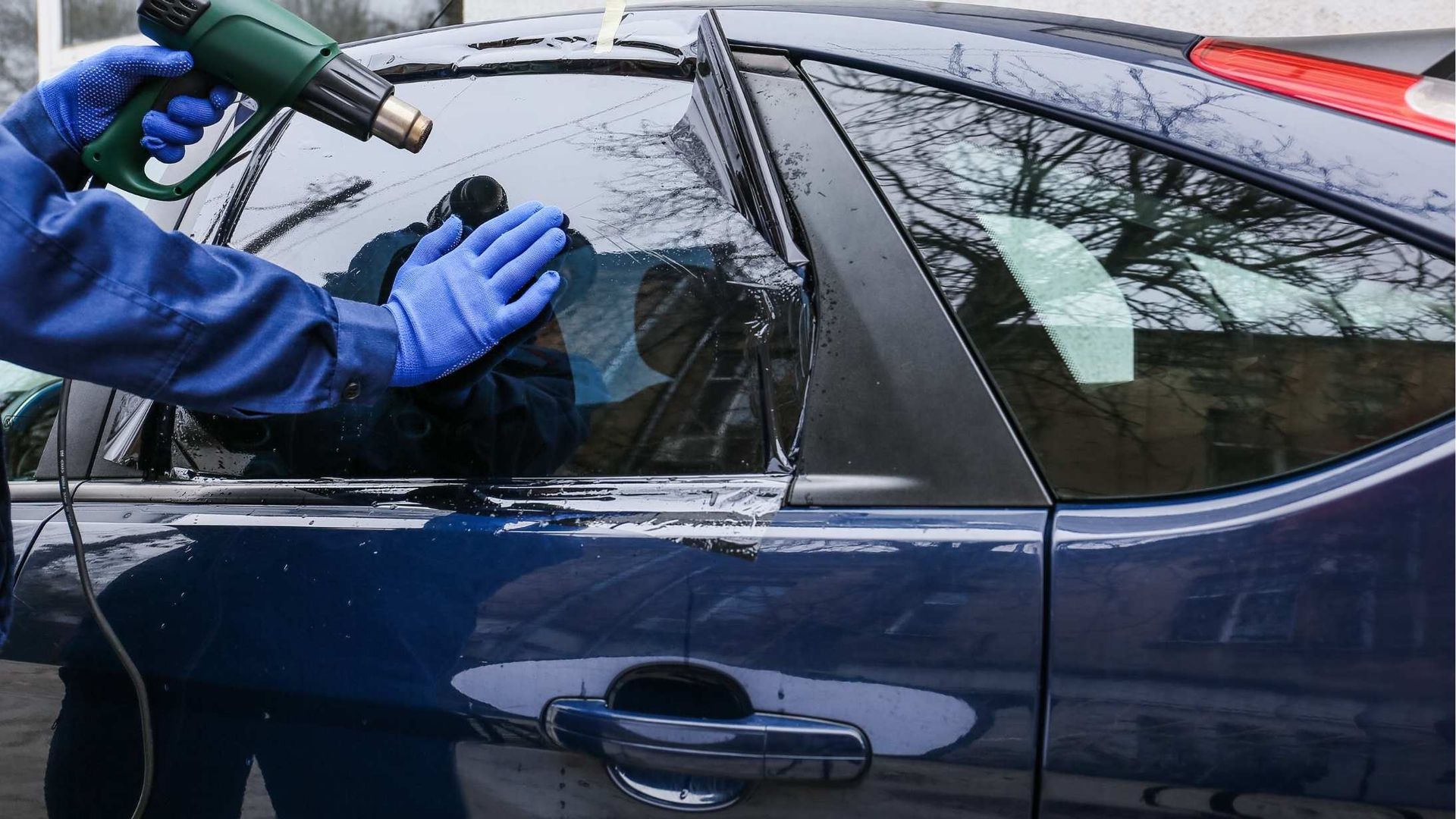 Person using a heat gun and gloved hands to remove film from a car window