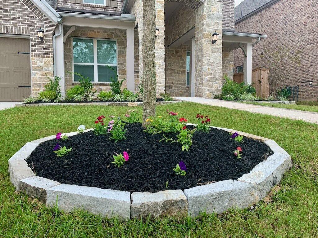 A garden with flowers and mulch in front of a house.