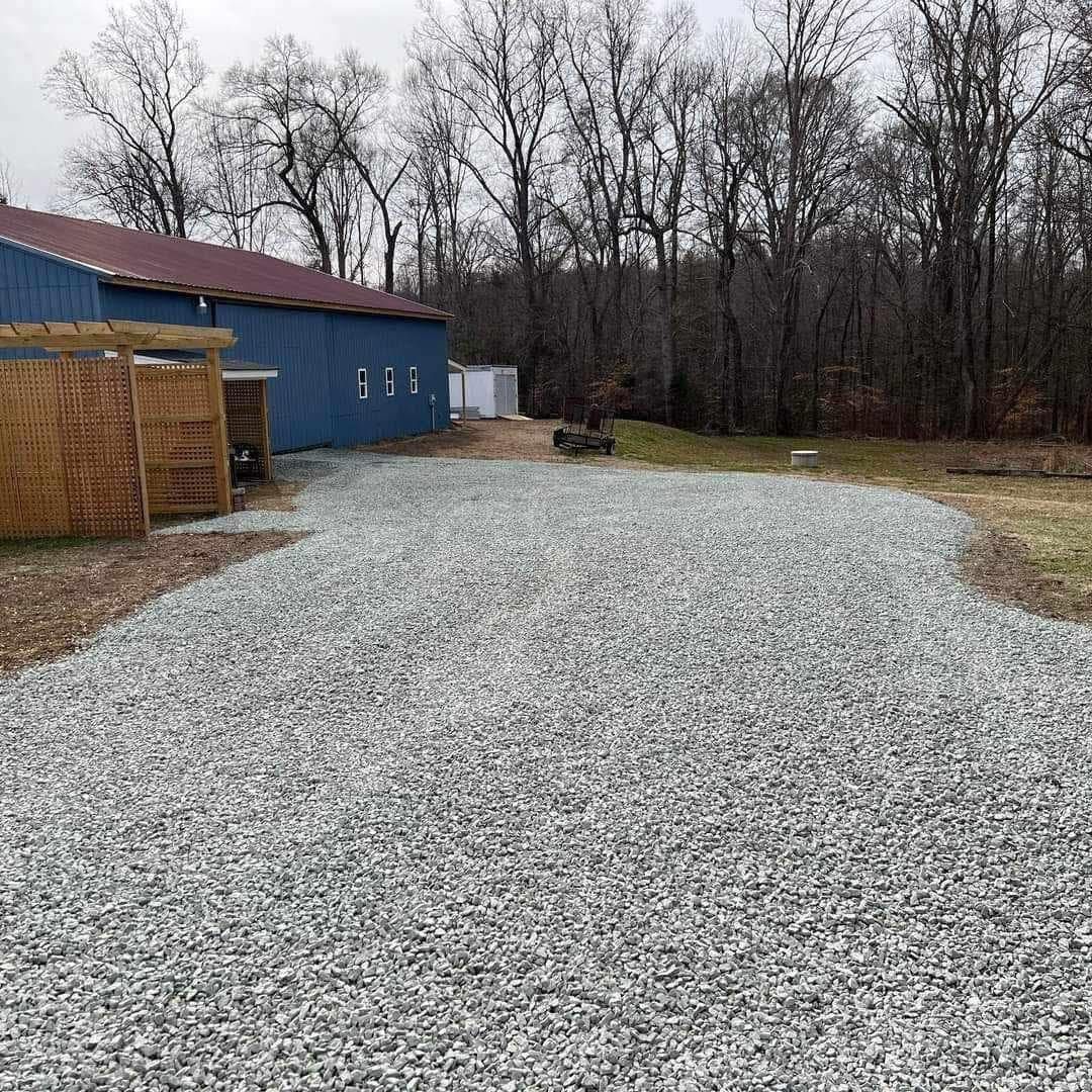 A gravel driveway leading to a blue building with trees in the background.