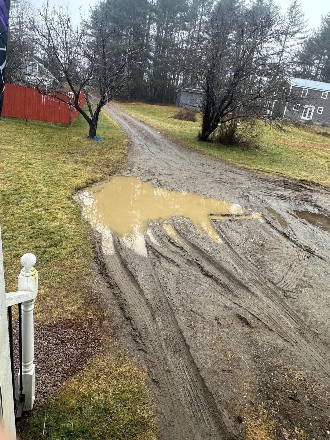 A muddy road with a puddle of water on the side of it.
