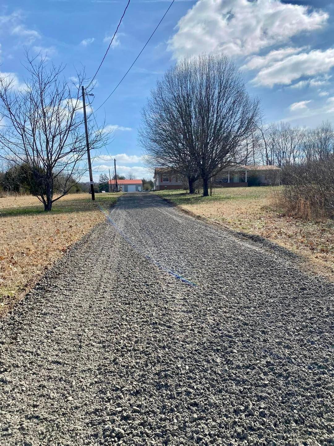 A gravel road leading to a house in the middle of a field.