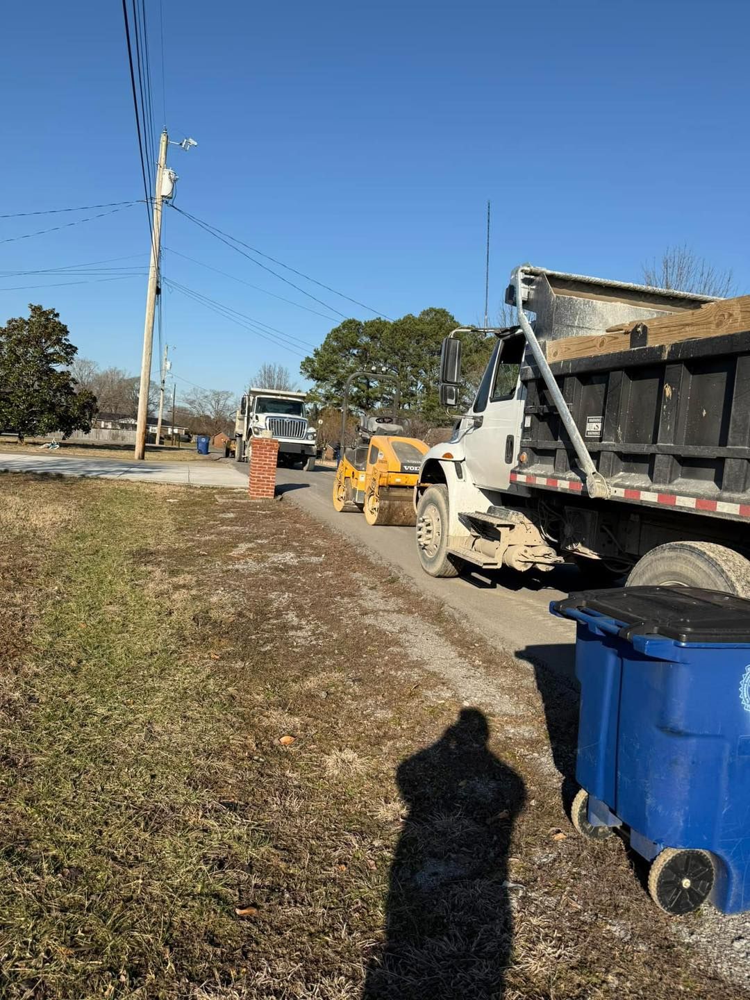 A dump truck is parked on the side of the road next to a blue trash can.