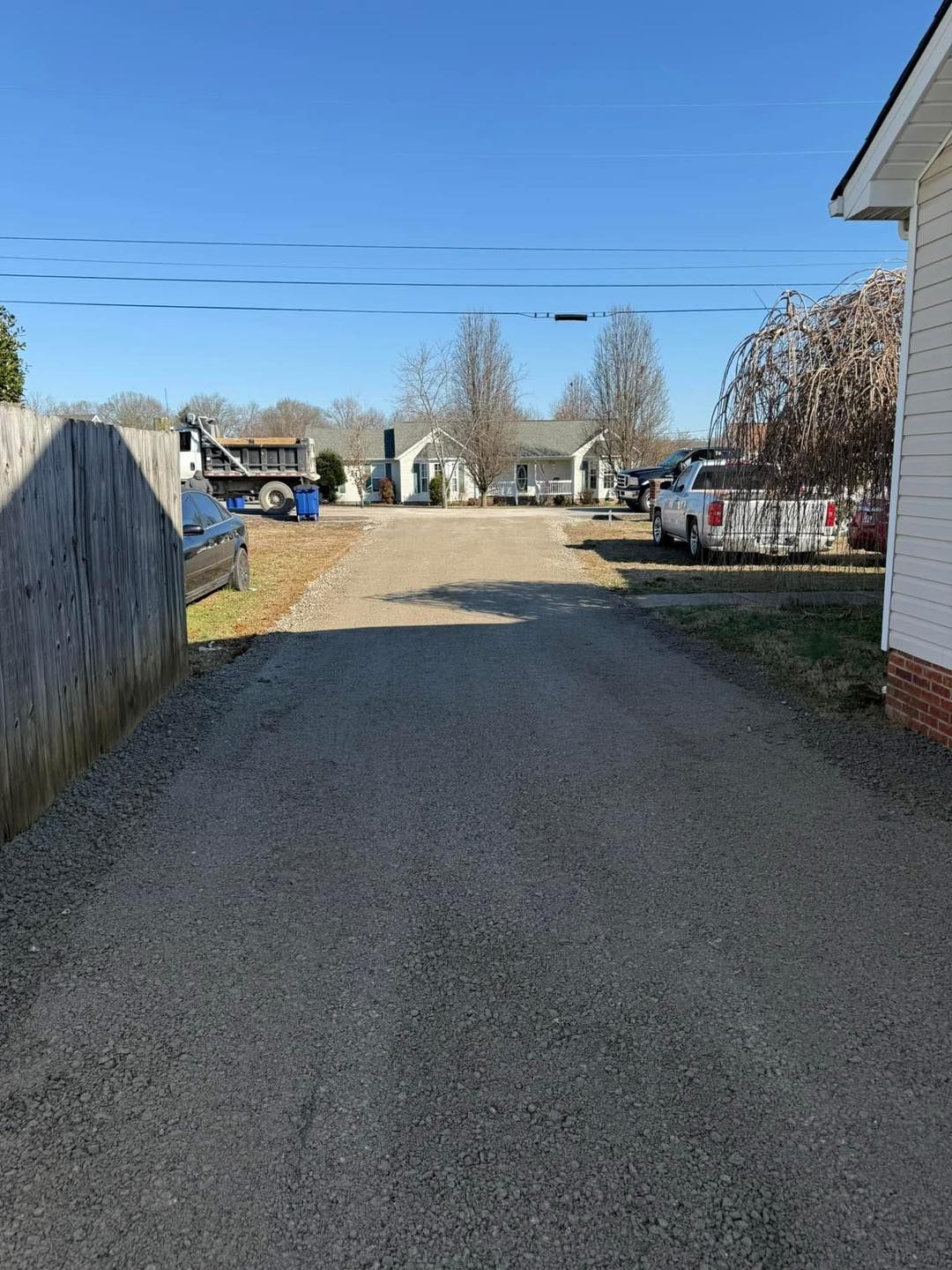 A driveway leading to a house with a fence and a few cars parked on the side of it.