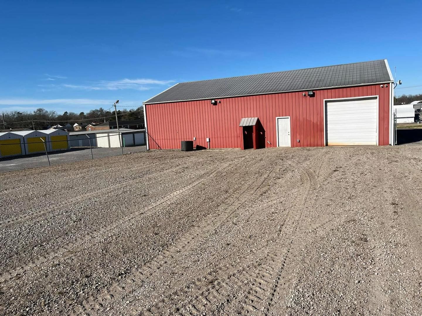 A red barn is sitting in the middle of a gravel lot.
