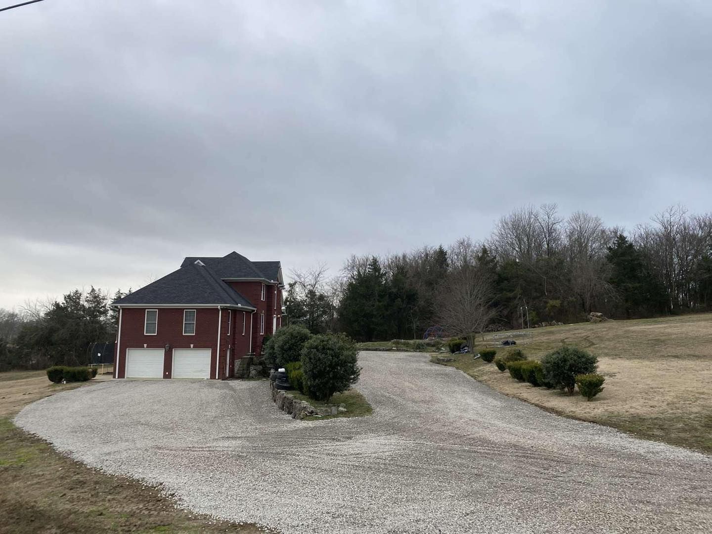 A red house with two garage doors is sitting on top of a gravel driveway.