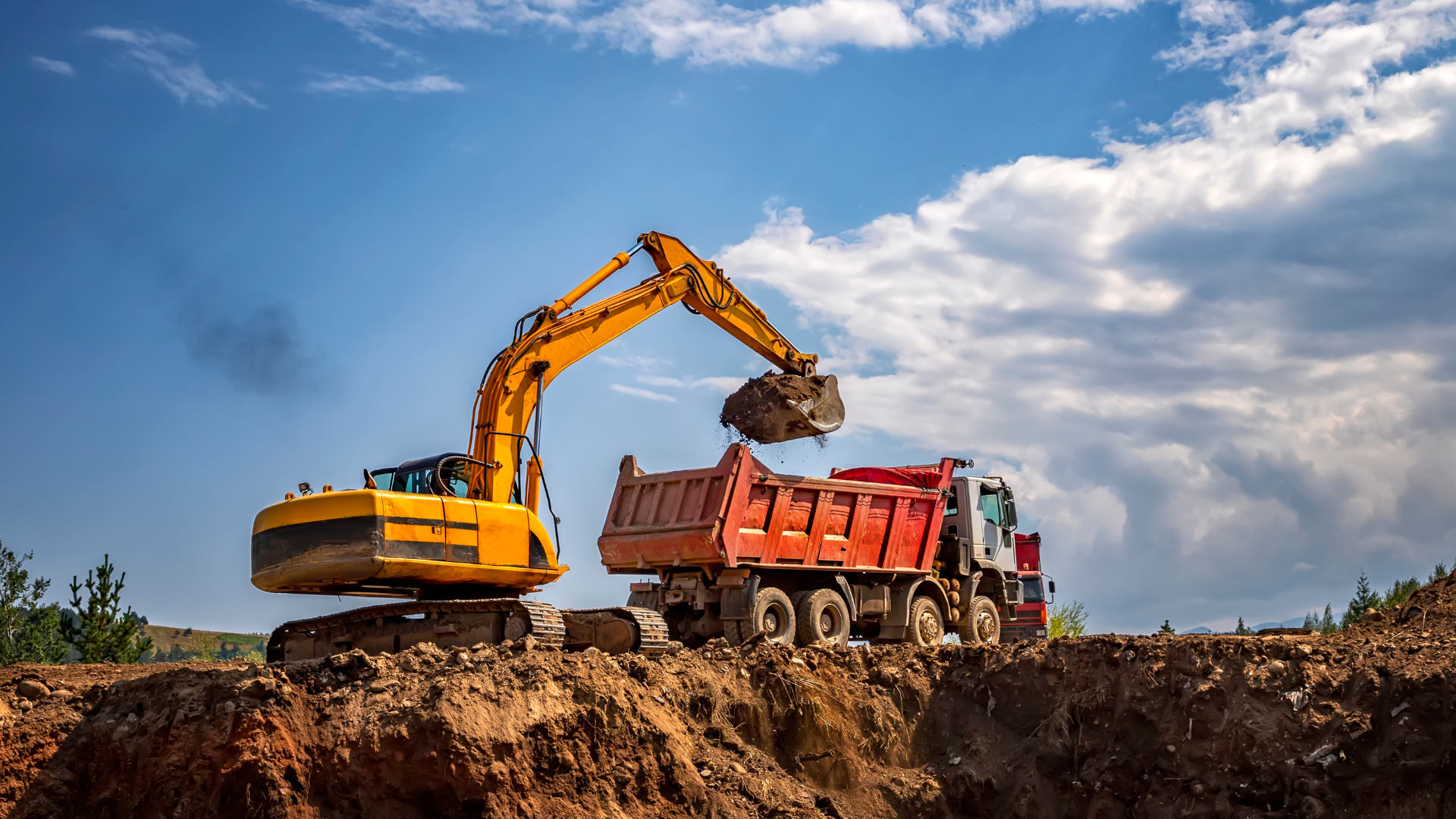 A yellow excavator is loading dirt into a dump truck.