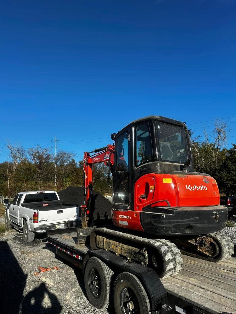 A red excavator is being towed by a truck on a trailer.