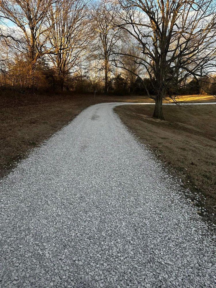 A gravel road going through a field with trees on the side.