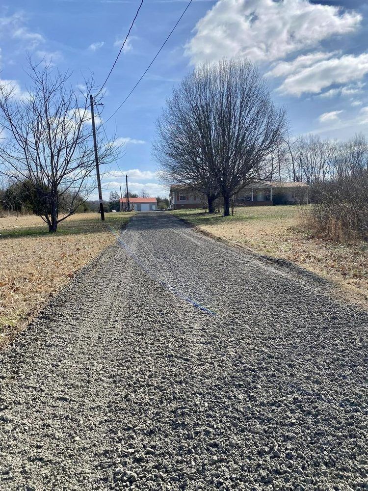 A gravel road leading to a house in the middle of a field.