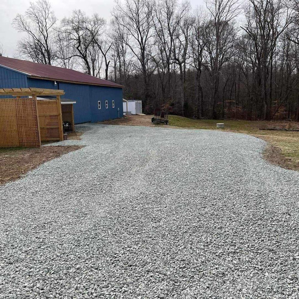 A gravel driveway leading to a blue barn in the woods.