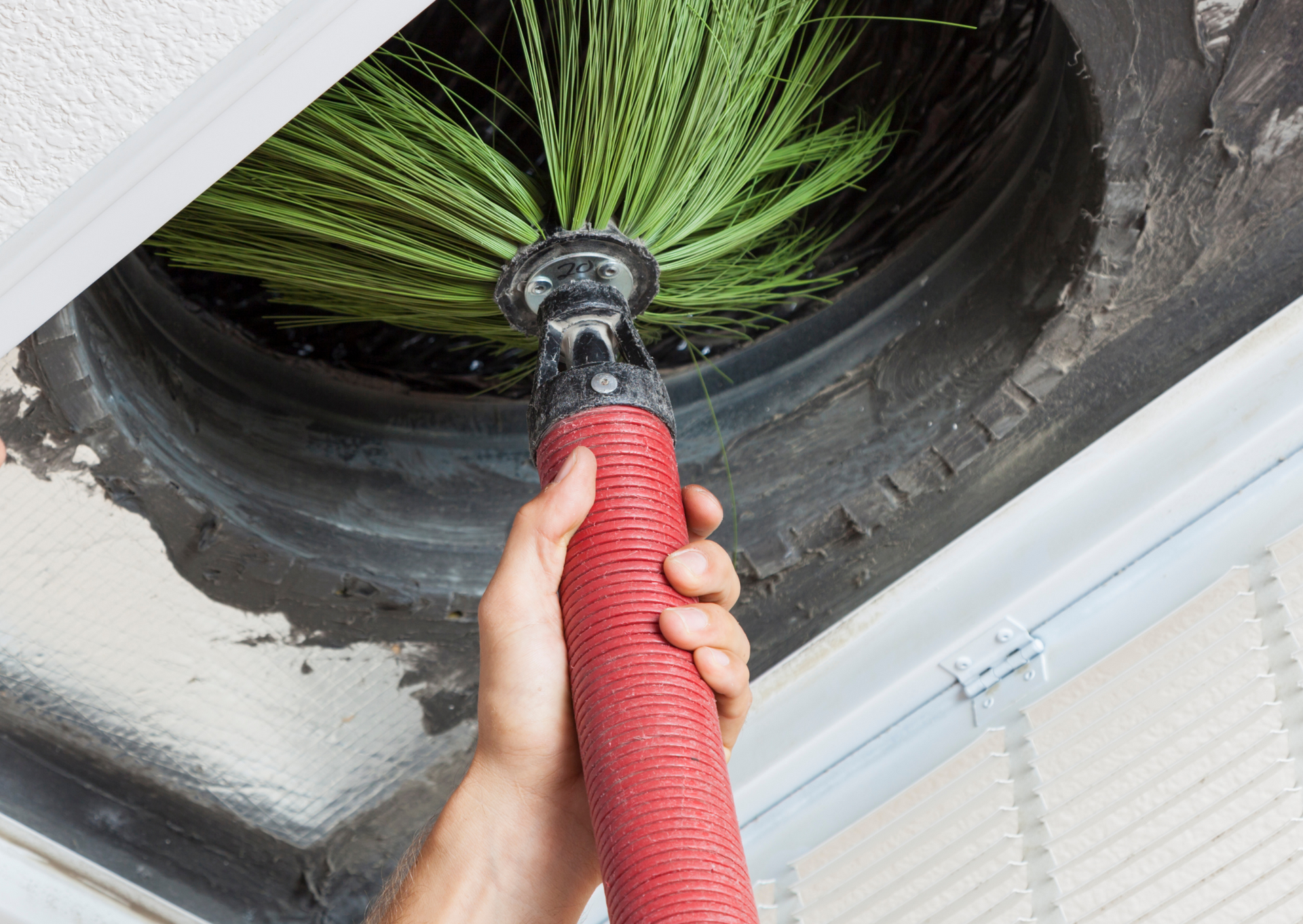 Hand holding a brush cleaning an air vent, removing dust and debris.