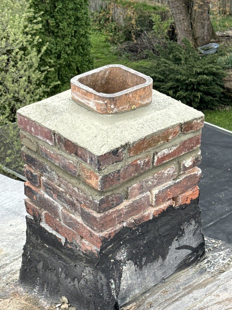 Brick chimney on a black roof, capped with a square clay flue.
