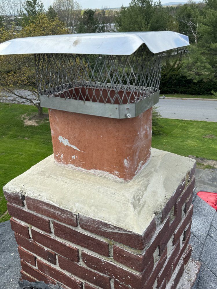 Brick chimney with a metal cap, on a roof. The chimney is square with a cement base.