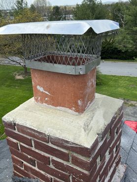 Brick chimney with a metal cap, on a roof. The chimney is square with a cement base.