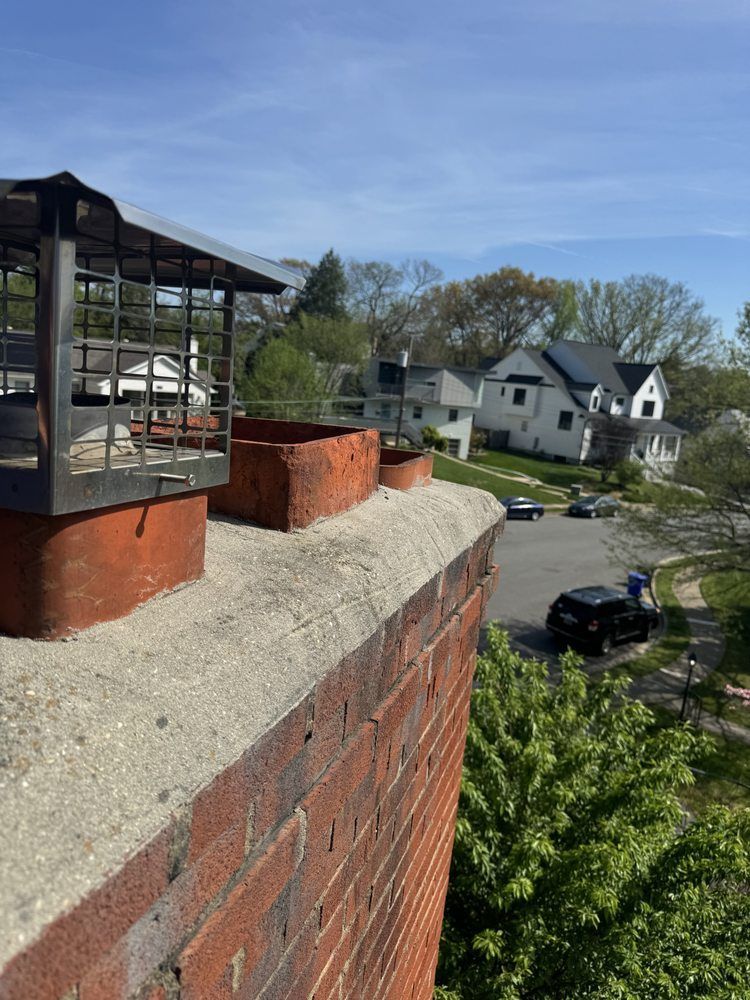 Red brick chimney with three flues and metal caps, overlooking a suburban neighborhood on a sunny day.