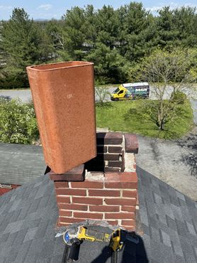 Chimney being repaired, brick and metal work visible. A yellow work truck is in the background.
