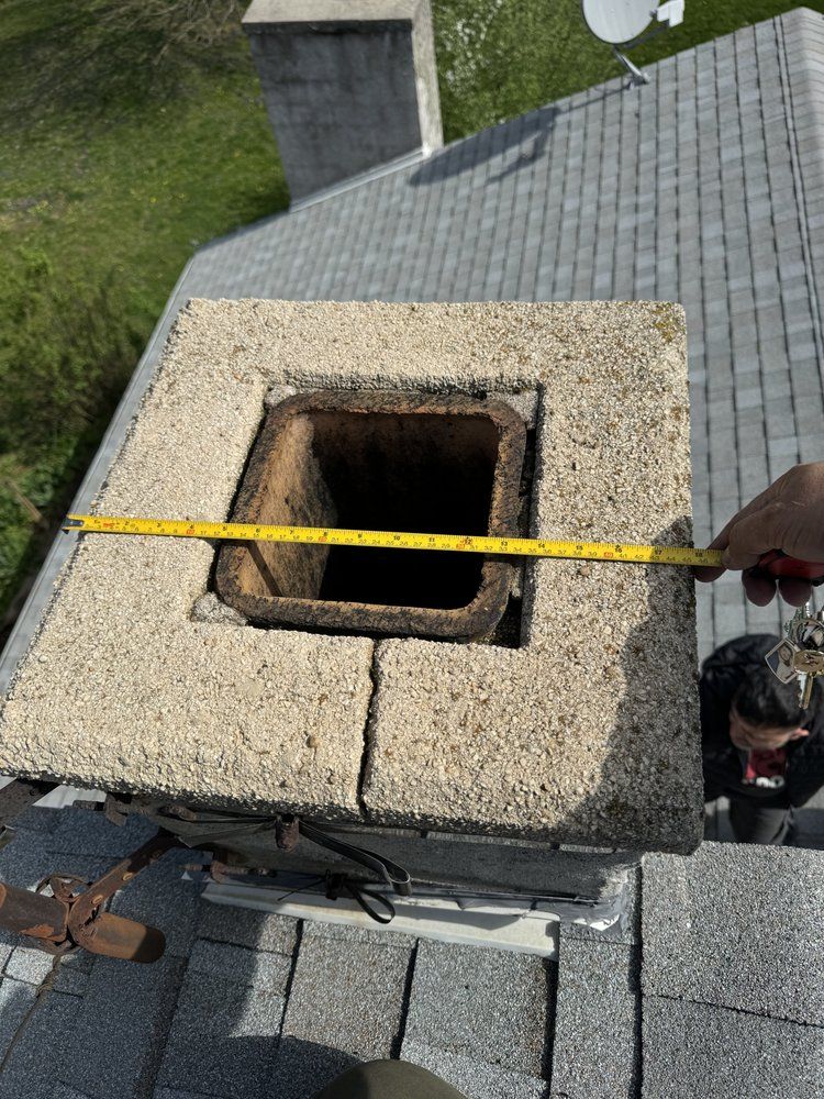 Measuring the top of a chimney on a gray shingled roof; a person's arm holds a measuring tape.