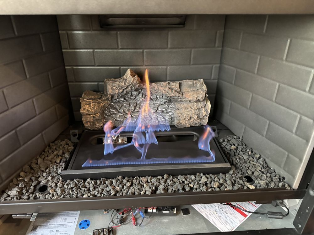 Gas fireplace with blue flames and artificial logs, surrounded by dark gray brick and rock.